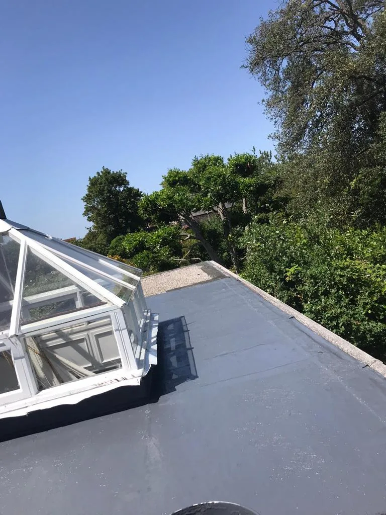 A finished grey flat roof with a glazed roof lantern under a blue sky