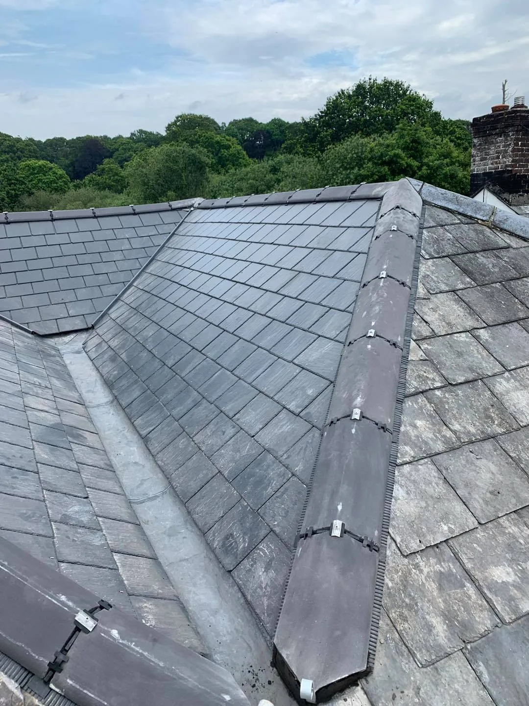 A new slate hipped roof with lead hip detail and trees behind