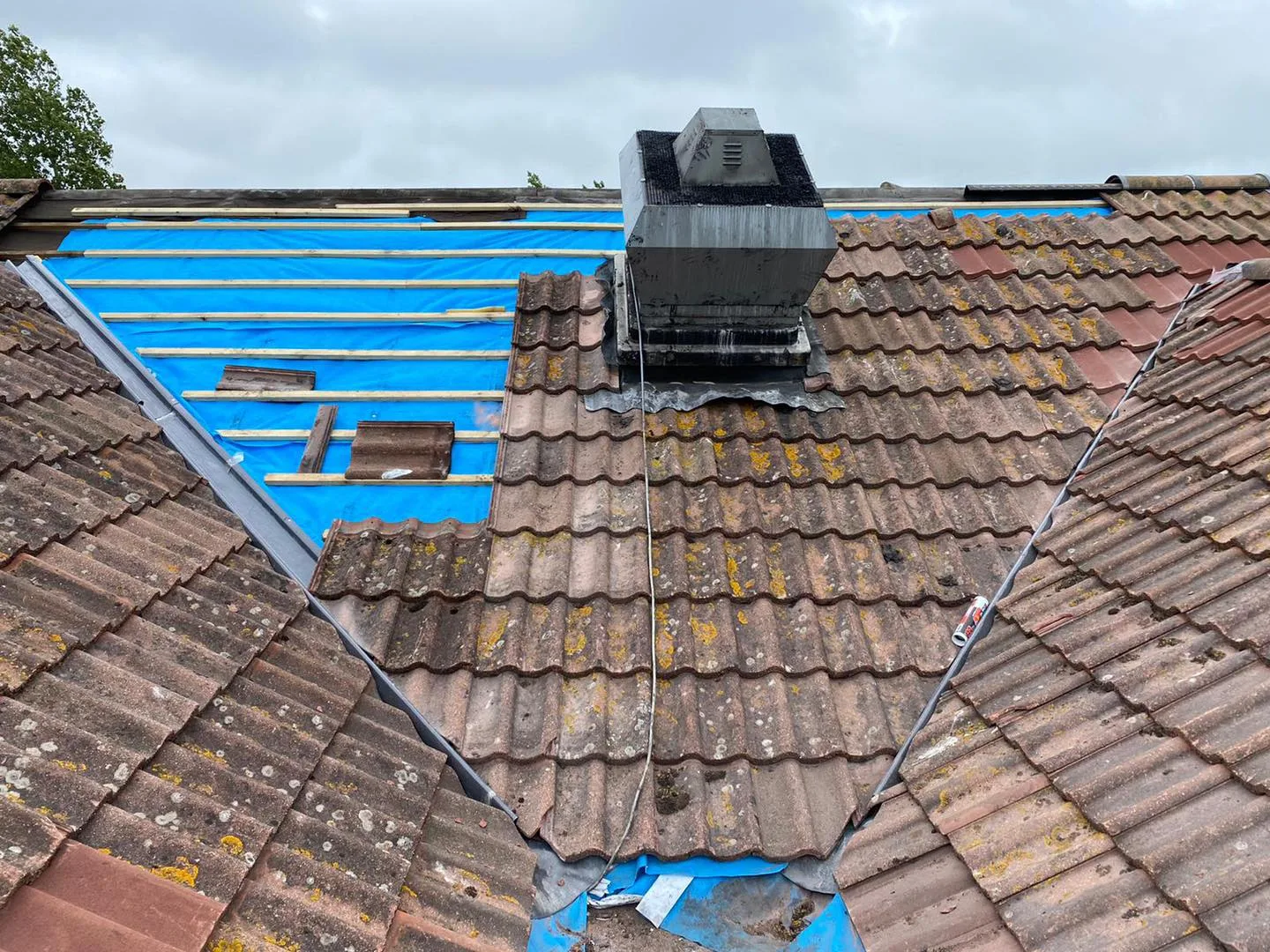 A roof half stripped to its blue membrane around a chimney stack